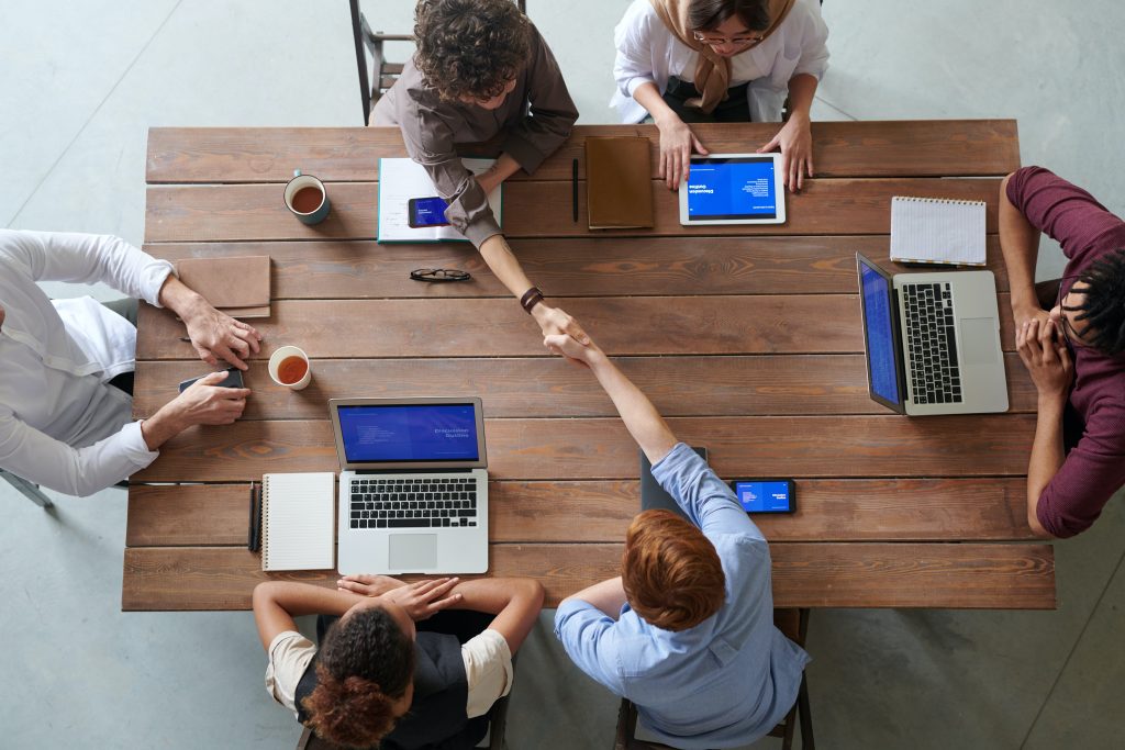 Cinq collaborateurs autour d'une table discutant, deux se serrent la main. Premiers pas dans le monde professionnel